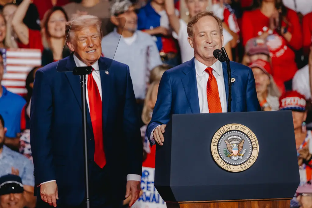 Two men in suits smile while standing behind a podium bearing the presidential seal, with a crowd of supporters in red and blue behind them