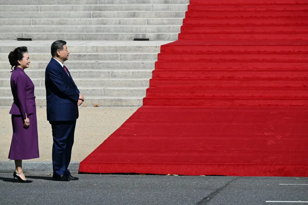 Chinese President Xi Jinping and First Lady Peng Liyuan stand before a red carpet at the base of a staircase